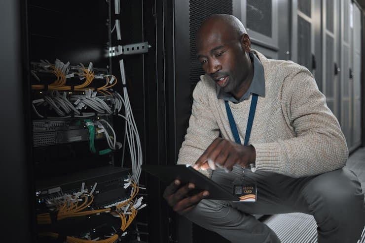 Technician with a tablet beside network cabling in a server room, illustrating Verbosec Internet dedicated internet