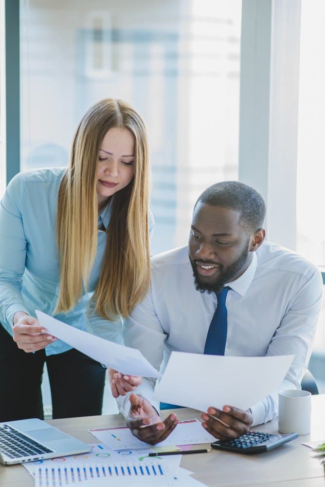 Two financial services professionals reviewing financial reports and charts during a client meeting
